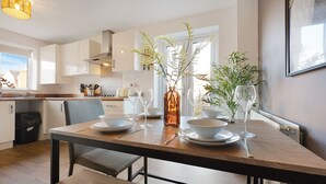 Una cocina moderna con armarios blancos, una mesa de comedor de madera dispuesta con platos, vasos y un florero con plantas.