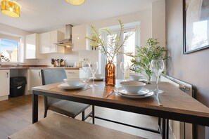 Eine moderne Küche mit weißen Schränken, einem Holzespeisetisch, der mit Tellern, Gläsern und einer Pflanze mit Grünpflanzen gedeckt ist.