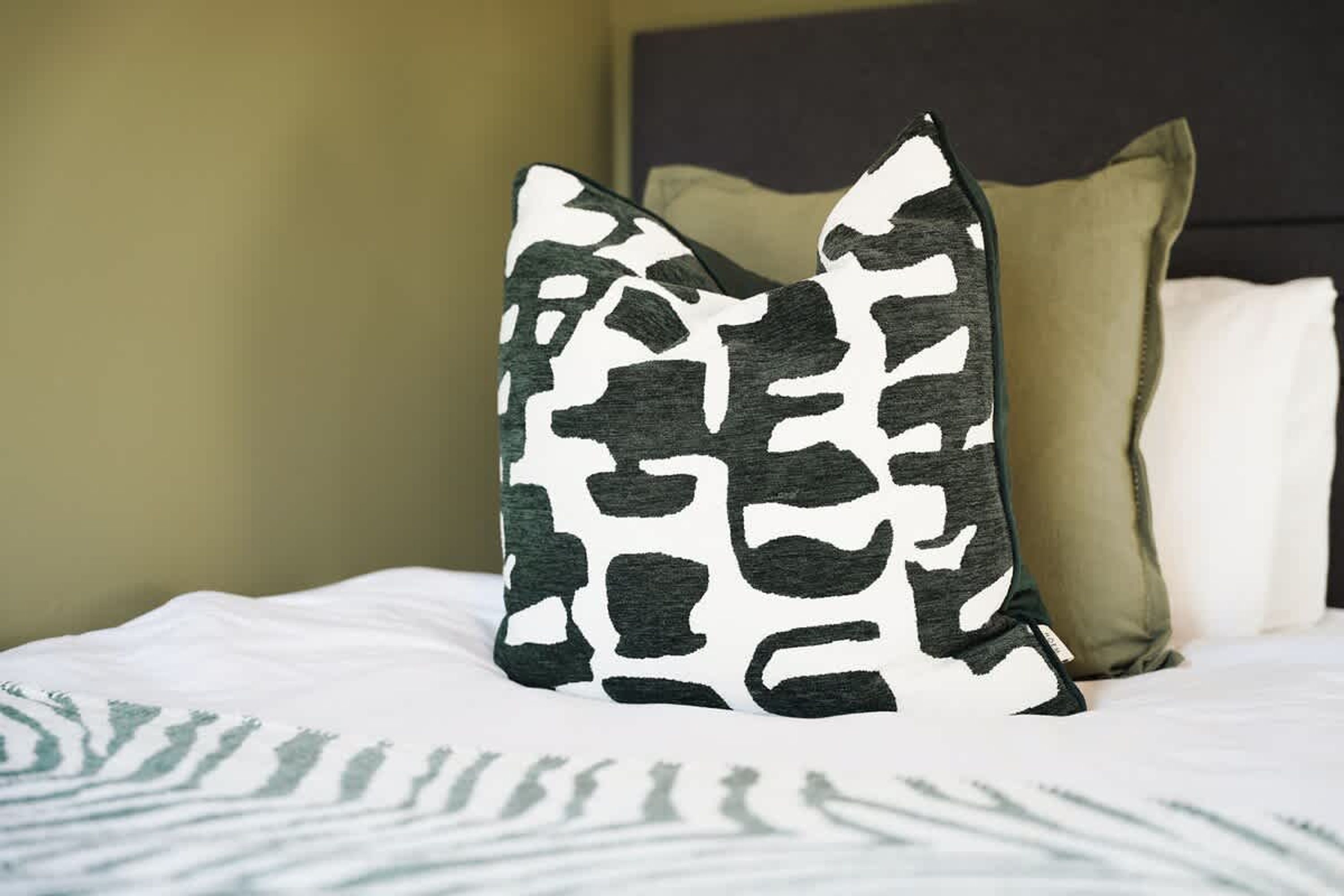 Una cama con un cojín estampado y otro liso.