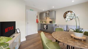 A modern living room with a flat-screen TV, a dining table with chairs, a kitchen area with cabinets and a microwave, and a potted orchid on the wall. - Central 2bed With Easy Access to Local Attractions (Barnard Castle)