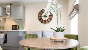 A modern kitchen with a round dining table, green upholstered chairs, a potted orchid, and a wall clock. - Central 2bed With Easy Access to Local Attractions (Barnard Castle)