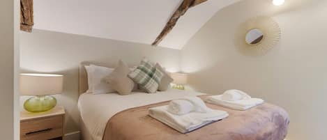 Un dormitorio con cama, almohadas, mesita de noche con lámpara y un espejo en la pared.