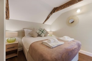 Un dormitorio con cama, almohadas, mesita de noche con lámpara y un espejo en la pared.