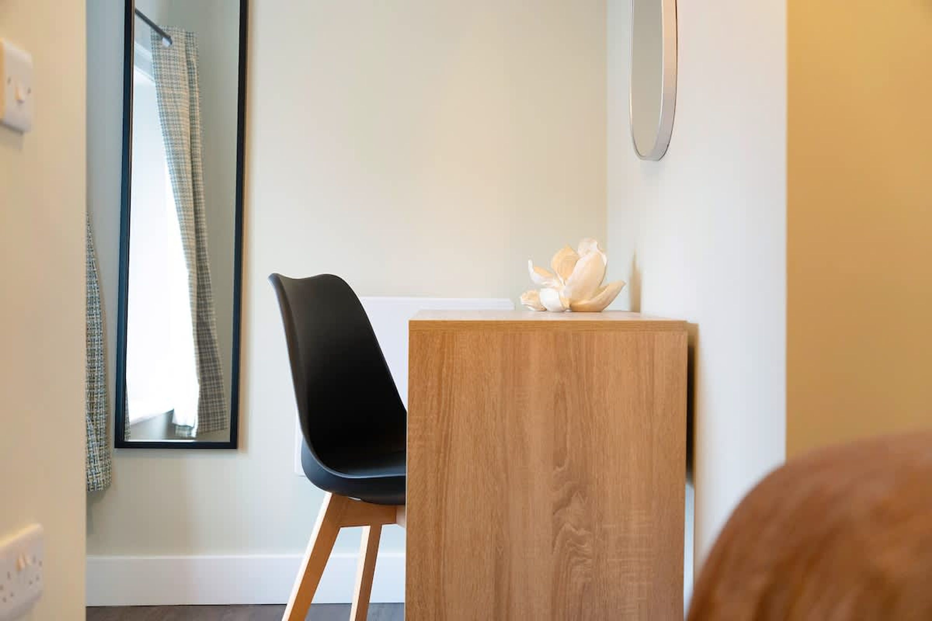Une chambre d’hôtel avec un bureau en bois, une chaise noire, un miroir et un objet décoratif posé sur le bureau.
