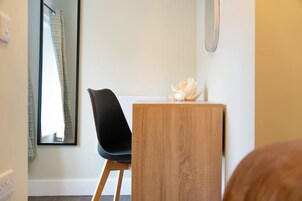 Habitación de hotel con un escritorio de madera, una silla negra, un espejo y un objeto decorativo sobre el escritorio.