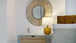 A bedroom with a bed, a bedside table with a lamp, a mirror, and a small plant.