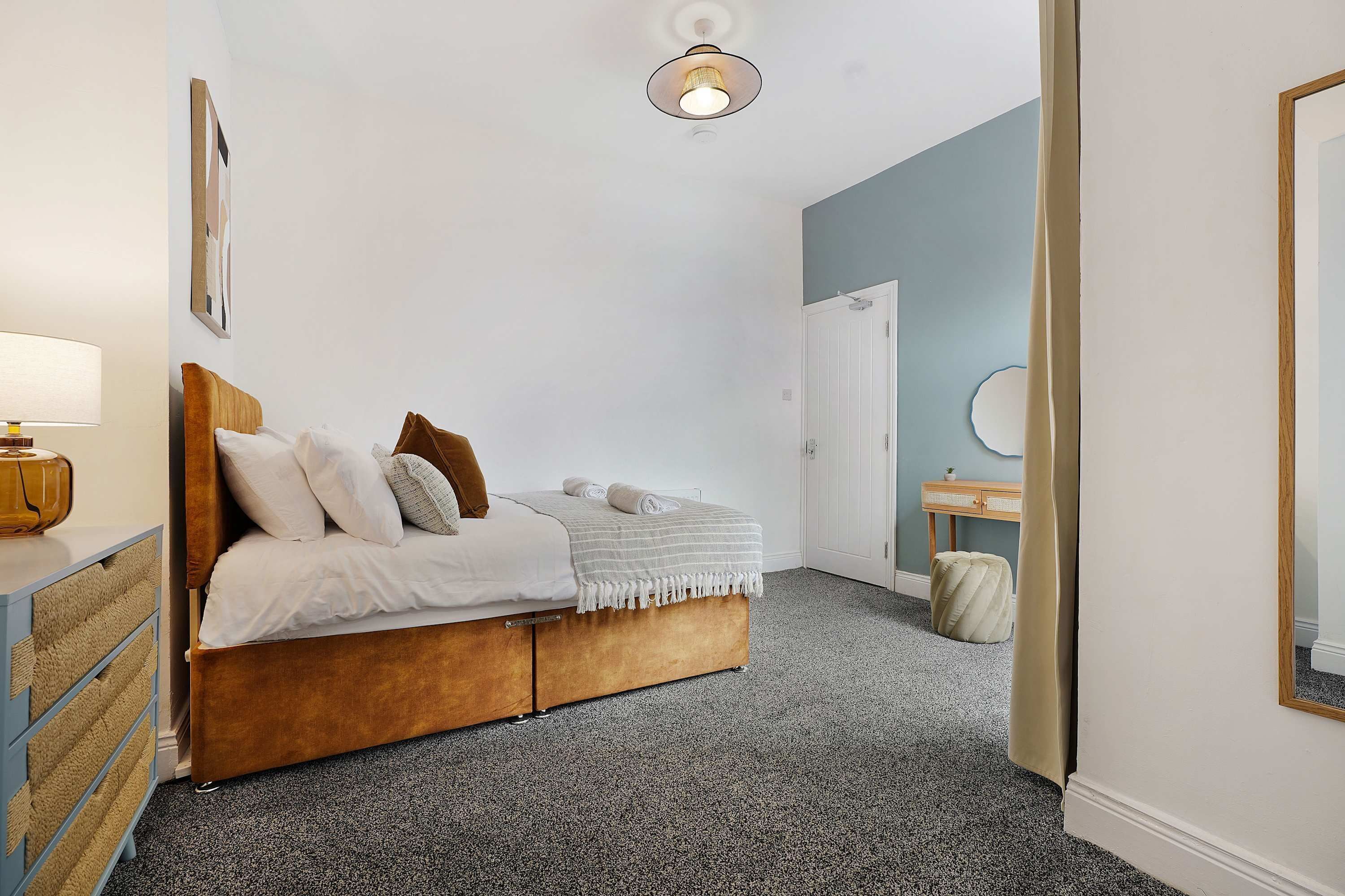 A bedroom with a bed, bedside table, lamp, and a door leading to another room.