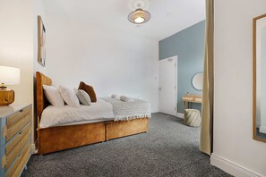Ein Schlafzimmer mit Bett, Nachttisch, Lampe und einer Tür zu einem anderen Raum.
