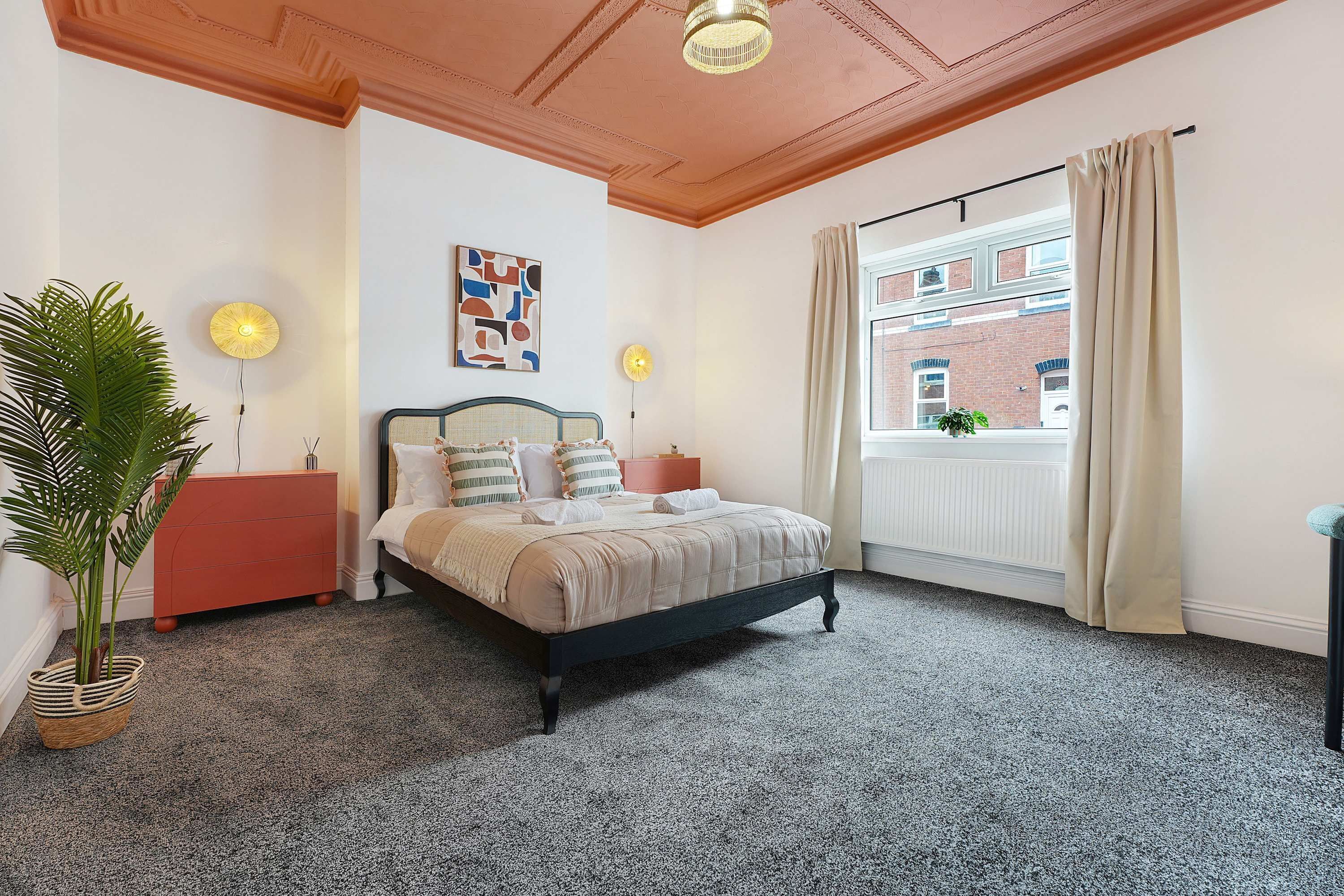 A bedroom with a bed, a dresser, a potted plant, a window with curtains, and a radiator.