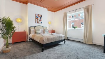 A bedroom with a bed, a dresser, a potted plant, a window with curtains, and a radiator.