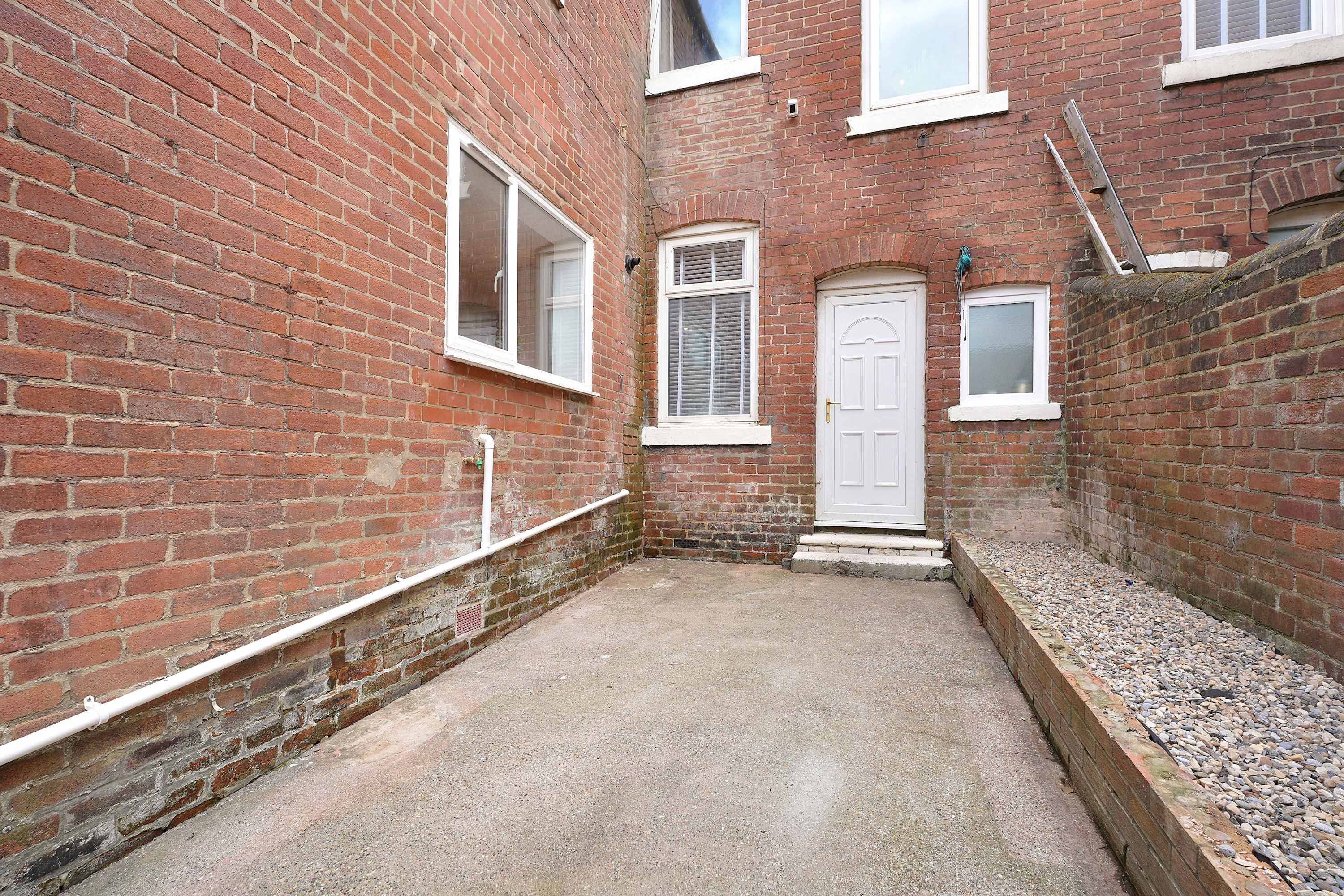 A narrow alleyway with a red brick building, a white door, and a small window.