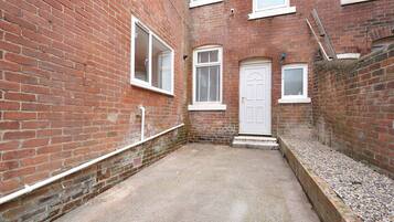 A narrow alleyway with a red brick building, a white door, and a small window.