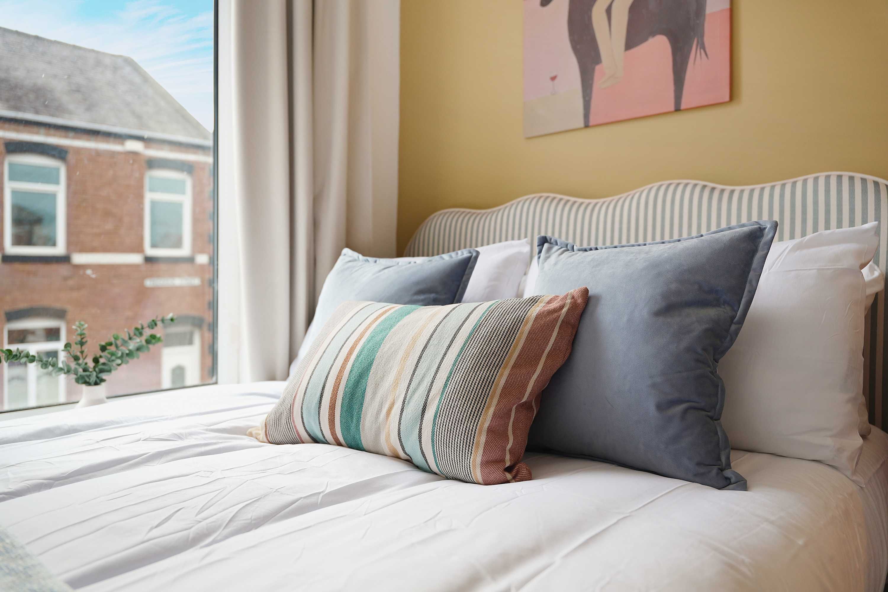 A bed with white bedding, two pillows, and a view of a building outside.
