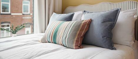 A bed with white bedding, two pillows, and a view of a building outside.
