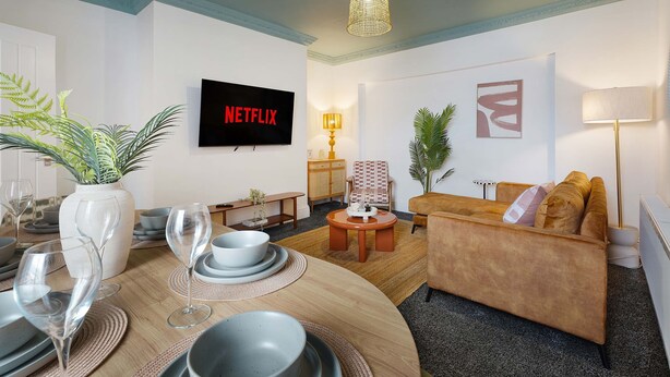 A modern living room with a flat-screen TV, a dining area with a table set for two, and a comfortable sofa.