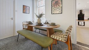 A dining area with a round table, chairs, and a bench. There are two framed artworks on the walls.