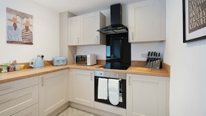 A modern kitchen with white cabinets, a black range hood, a built-in oven, a toaster, and a knife block.
