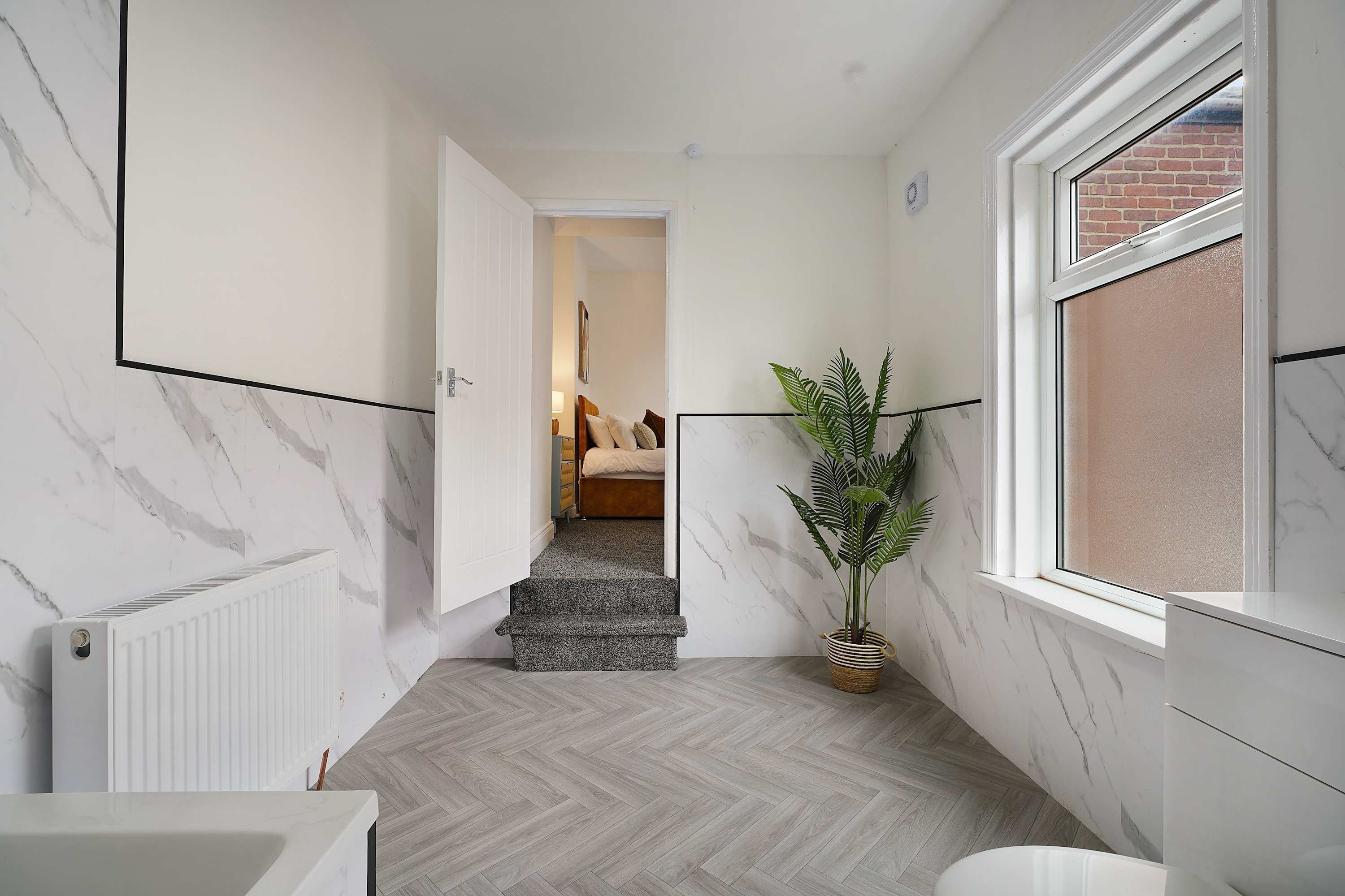 A hallway with a marble wall, a radiator, a potted plant, and a window with a view of a brick wall.