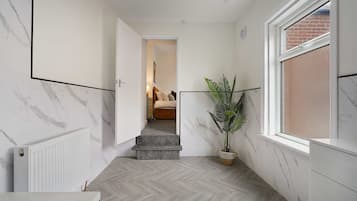 A hallway with a marble wall, a radiator, a potted plant, and a window with a view of a brick wall.