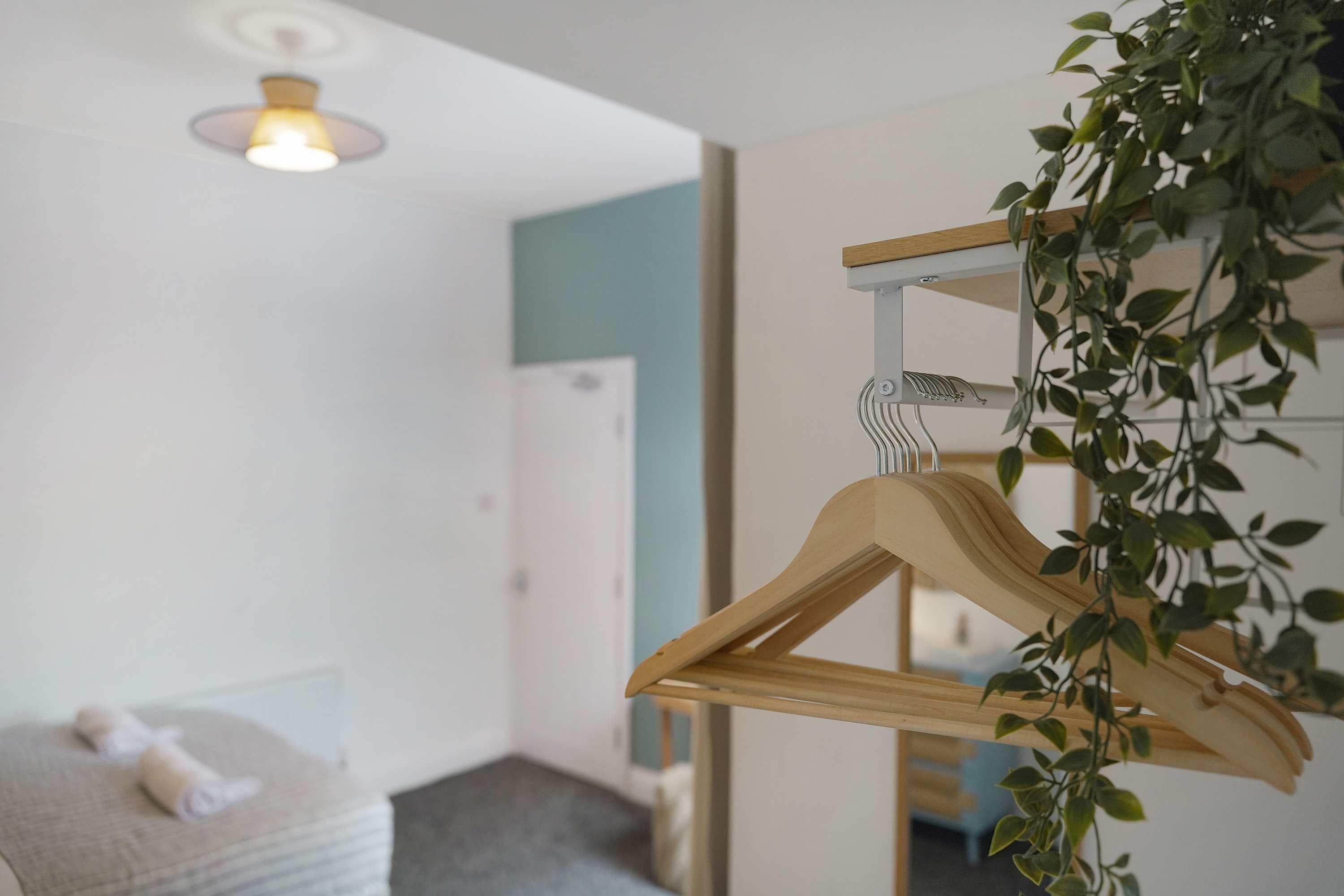 A room with a hanging wooden hanger, a bed, a wall-mounted light fixture, and a door.