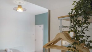 Una habitación con una percha de madera, una cama, una lámpara fijada a la pared y una puerta.