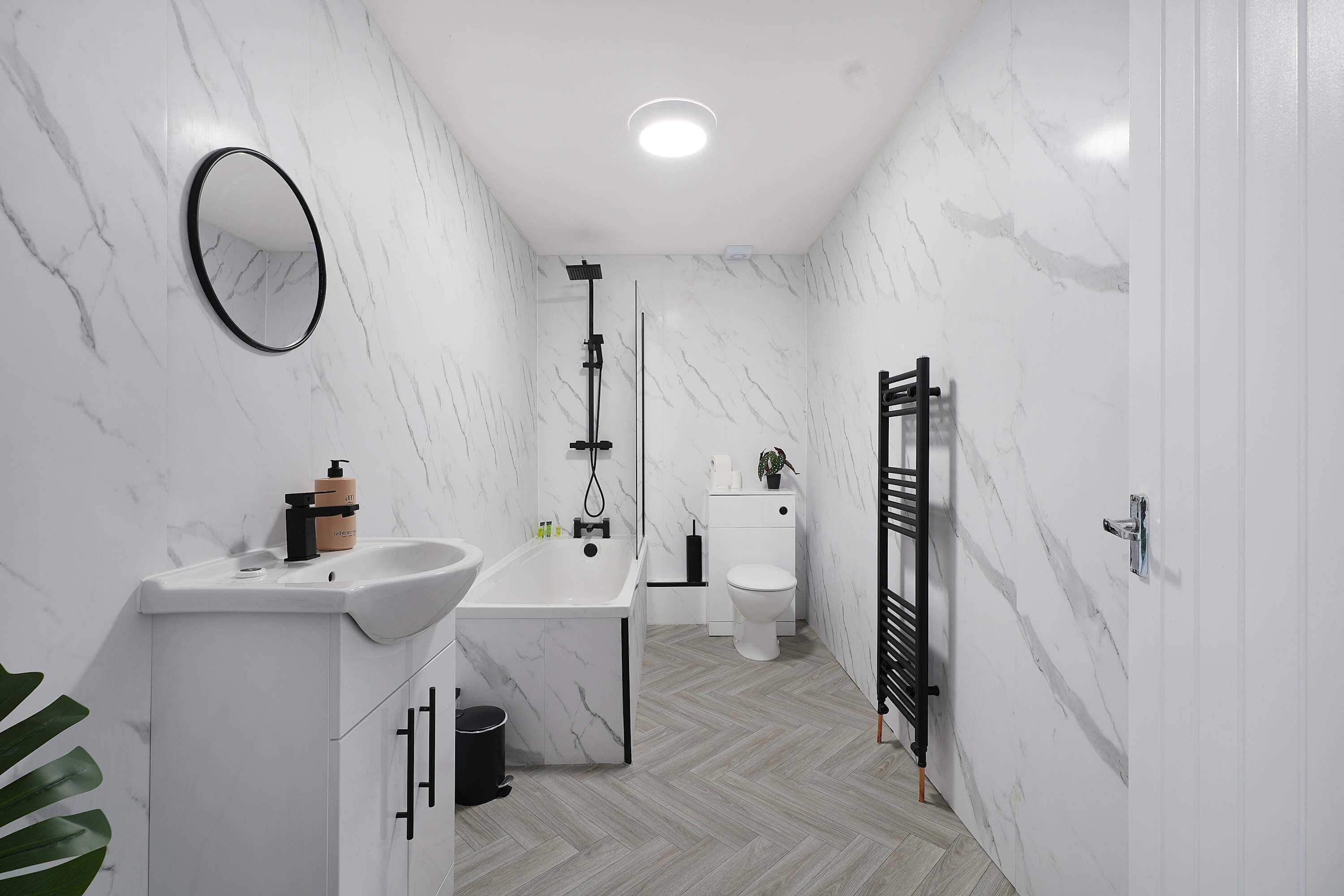 A bathroom with a white marble wall, a sink, a toilet, and a shower area.