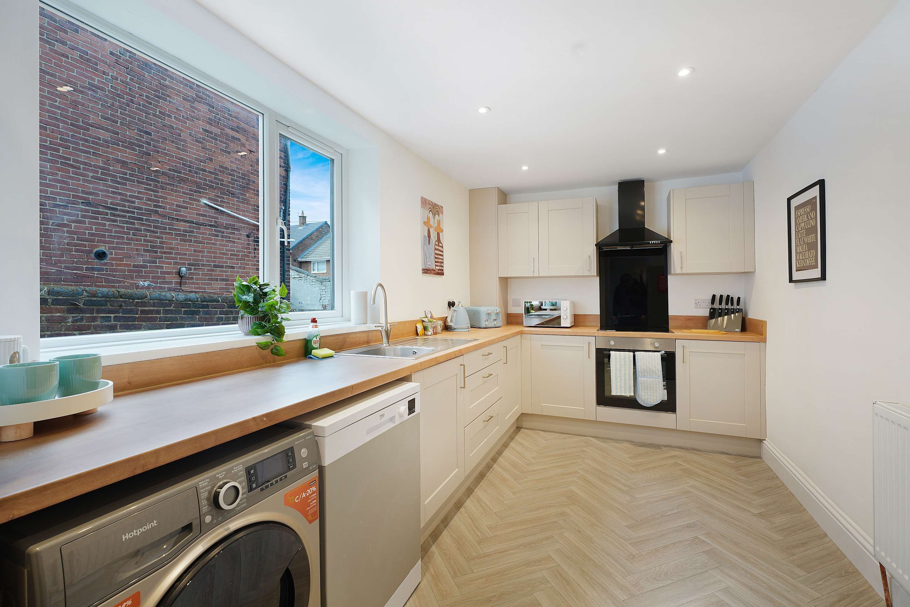 A modern kitchen with a dishwasher, oven, and a window overlooking a brick building.