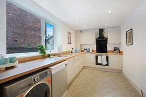 A modern kitchen with a dishwasher, oven, and a window overlooking a brick building. - Beachside 4BR Seaham Home by Stay With Us (Seaham)