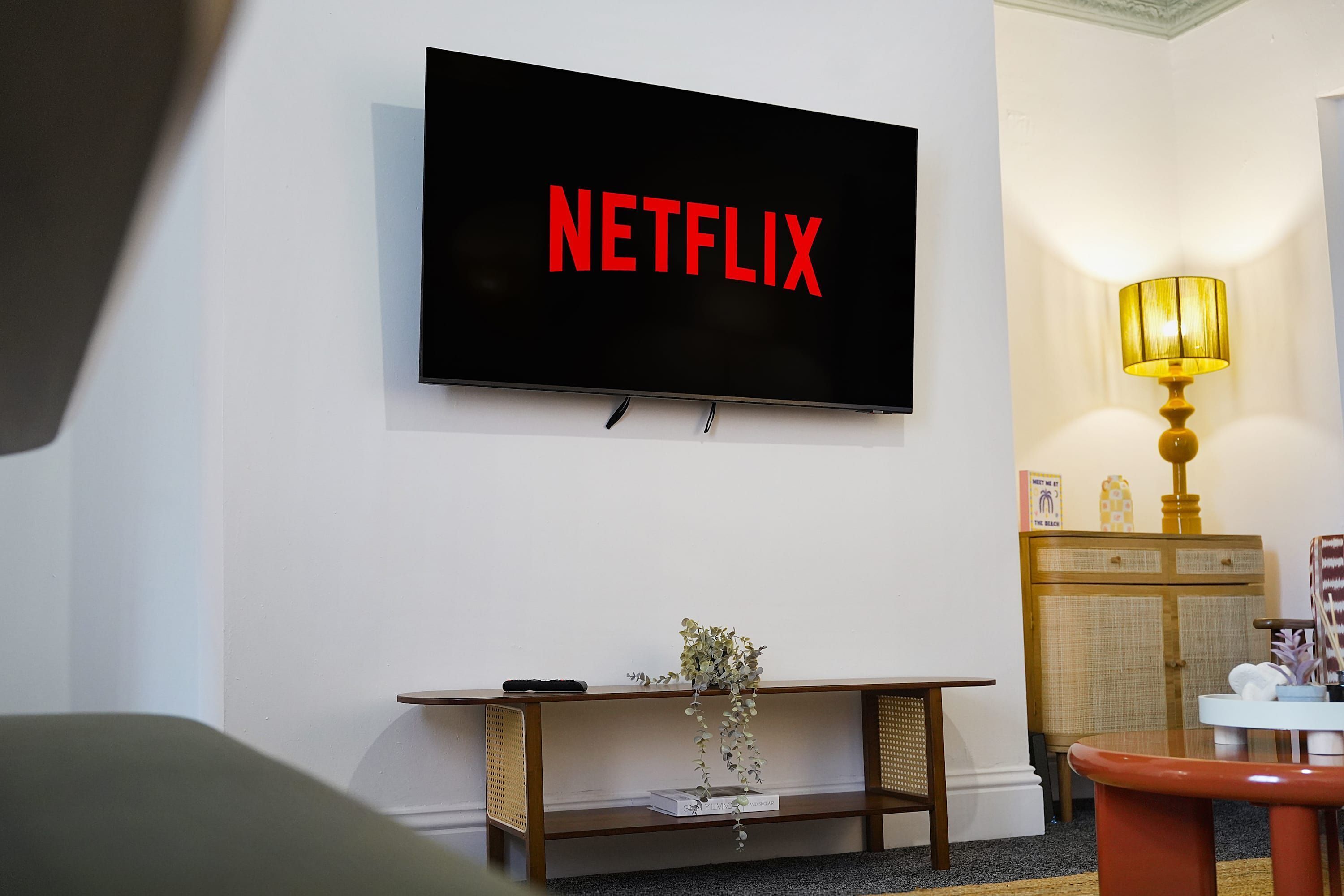 A living room with a television mounted on the wall displaying the Netflix logo.