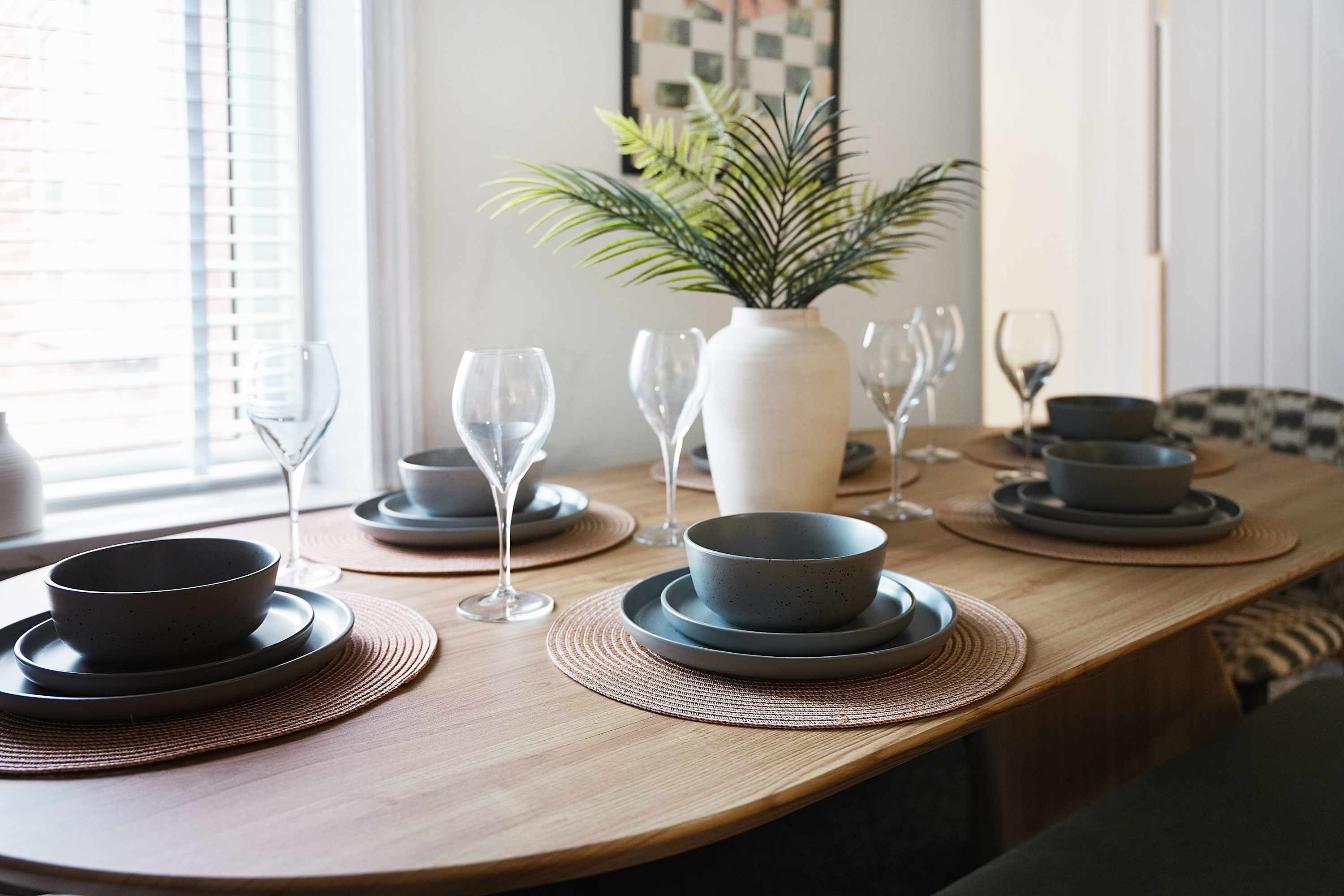 A dining table with plates, bowls, and wine glasses set for a meal.