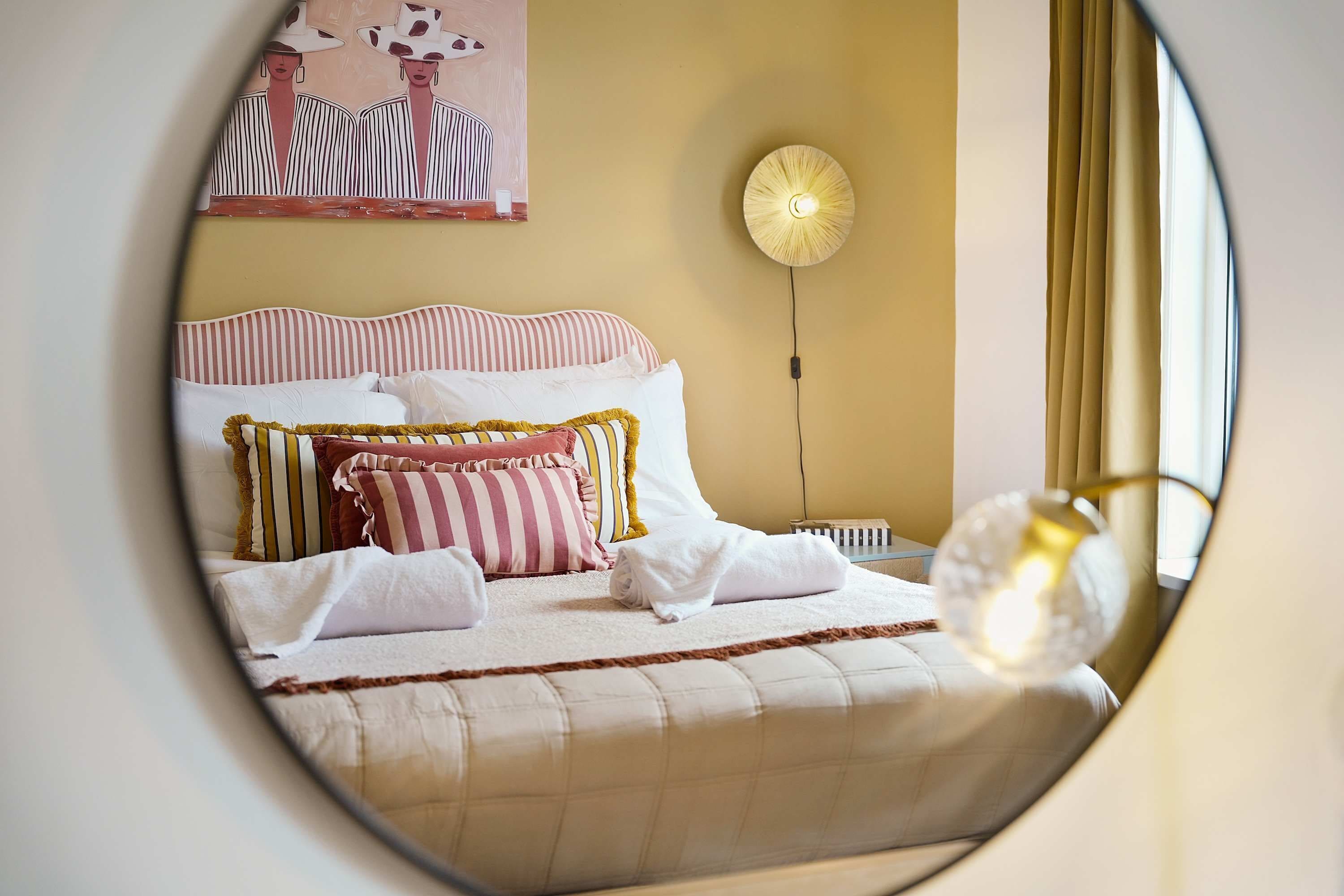 A bed with striped bedding, a bedside lamp, and a painting on the wall.