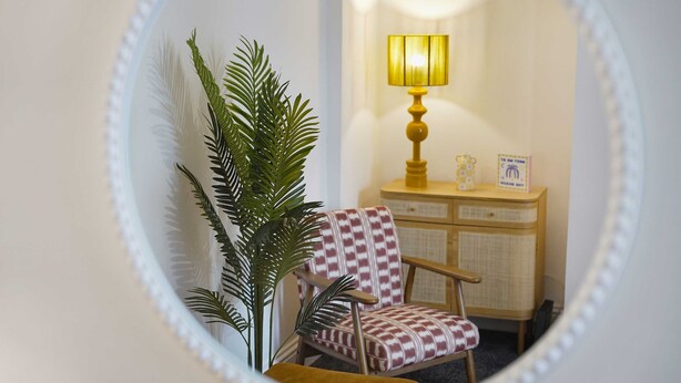 Una habitación con un espejo que refleja una silla, una lámpara y un armario.