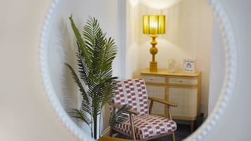A room with a mirror reflecting a chair, a lamp, and a cabinet.