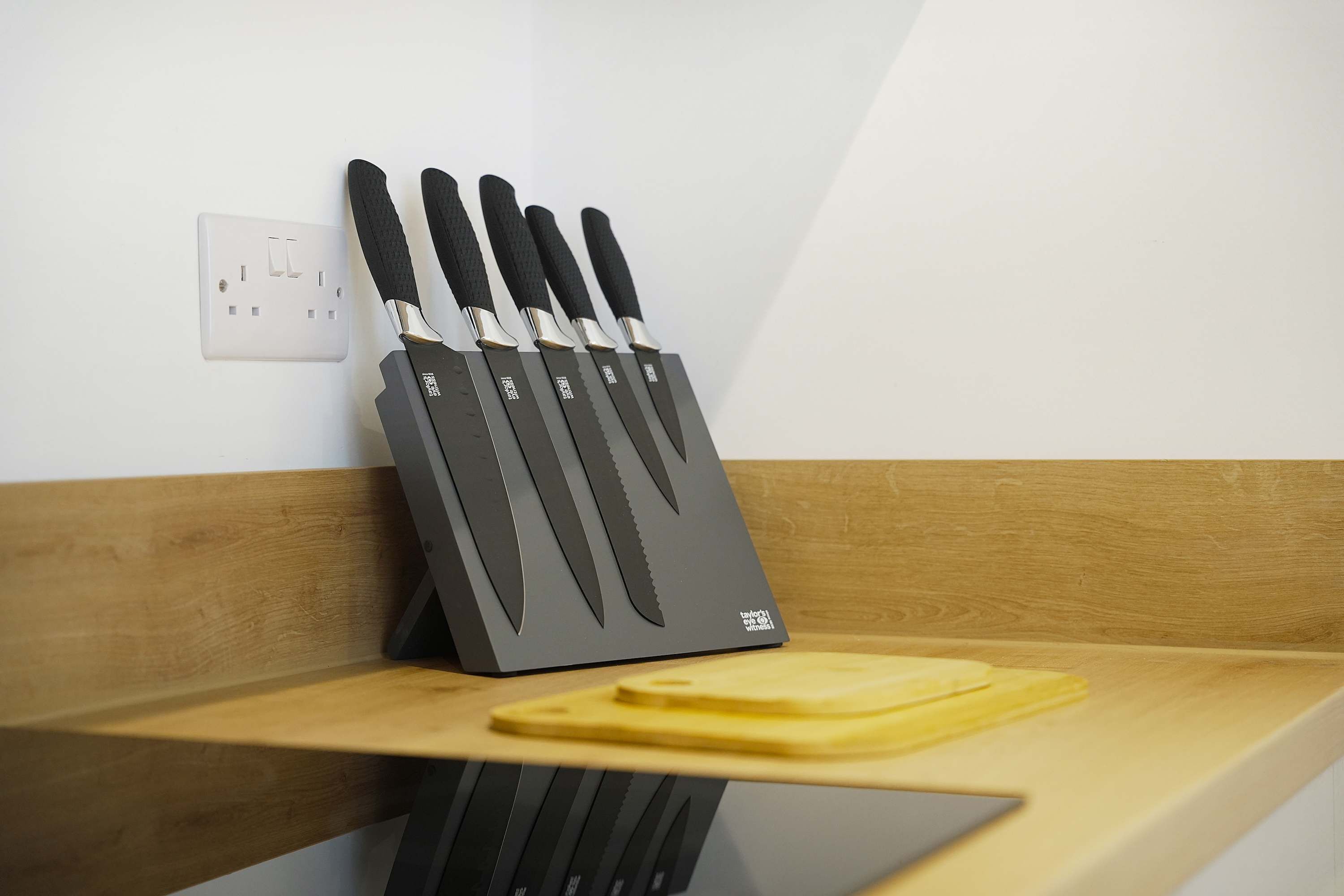 Ein Messerblock mit sechs Messern auf einer hölzernen Ablage vor einer weißen Wand.
