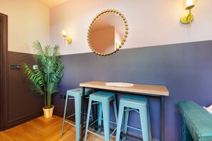 Ein Zimmer mit einem Holztisch, zwei Hocker, einem Spiegel und einer Topfpflanze.