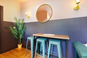 Una habitación con un escritorio de madera, dos taburetes, un espejo y una planta en maceta.