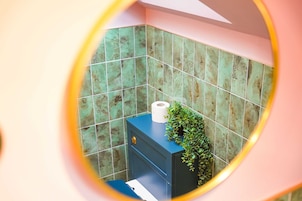 Un baño con azulejos verdes, un mueble azul y un rollo de papel higiénico.