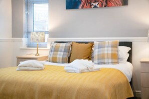 Cama bem arrumada com edredom amarelo, duas almofadas e duas toalhas dobradas.