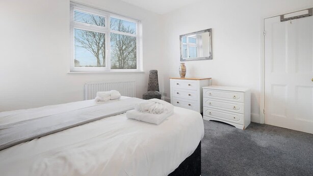A bedroom with a bed, two bedside tables, a dresser, a mirror, and a window with blinds. - 3 Bedroom in Haughton Road With Free Wifi (Darlington)