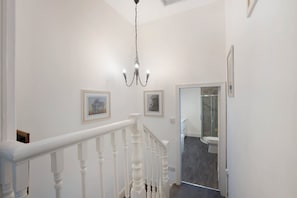 Eine Treppe mit weißen Spindeln führt zu einem Badezimmer mit einer Duschkabine aus Glas.