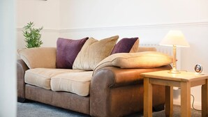 A brown leather sofa with cushions, a small wooden side table with a lamp, and a potted plant. - 3 Bedroom in Haughton Road With Free Wifi (Darlington)