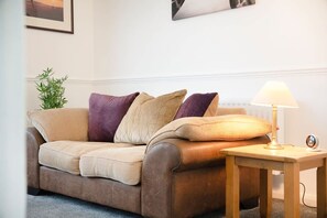 Ein braunes Ledersofa mit Kissen, ein kleiner Holztisch mit einer Lampe und ein Blumentopf.