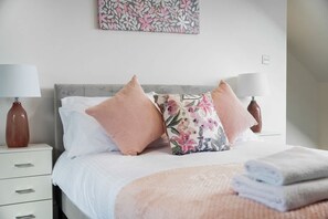A neatly made bed with a floral pillow, a white bedside table with a lamp, and a wall-mounted artwork. - 4BR South Shields Stay Sleeps 8 by Stay With Us (South Shields)