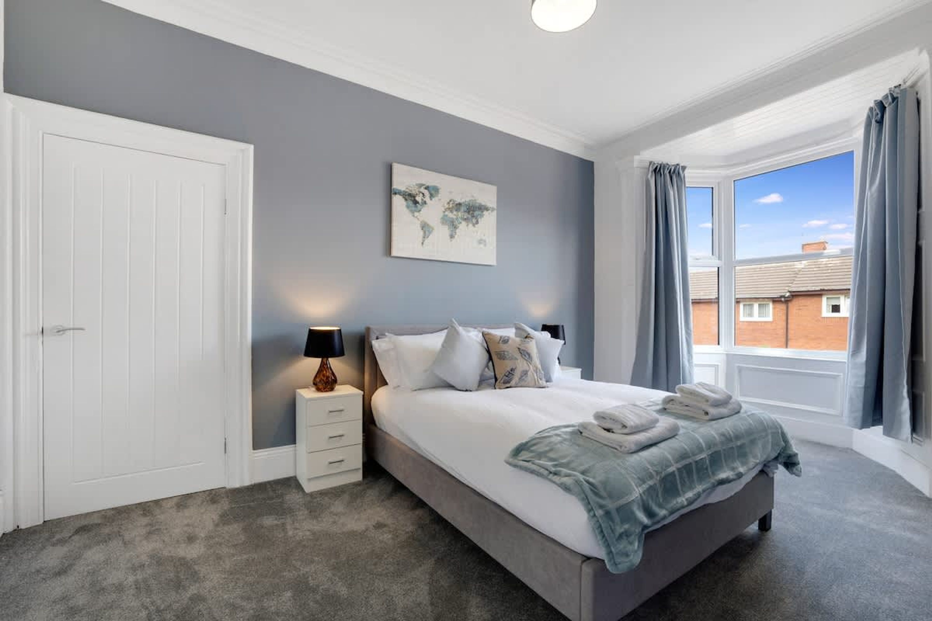 A bedroom with a bed, a nightstand, a world map artwork, and a window with curtains.