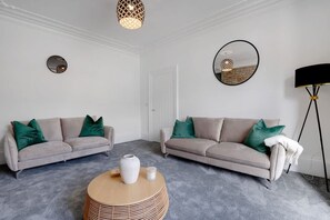 Ein modernes Wohnzimmer mit zwei Sofas, einem Couchtisch, einer Stehlampe und einem Spiegel an der Wand.