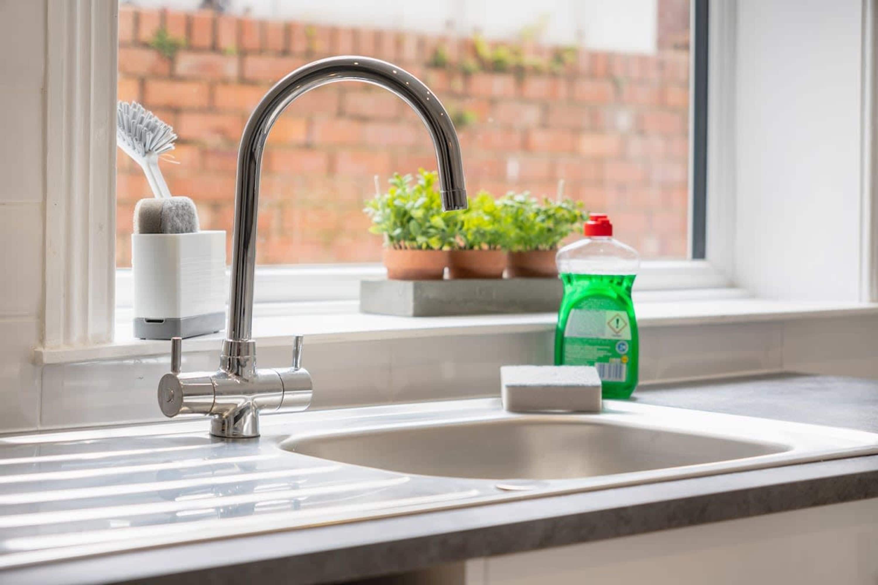 Un évier de cuisine avec un robinet, une bouteille de liquide vaisselle, une éponge et un égouttoir.