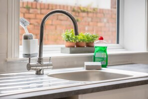 Eine Spüle mit Wasserhahn, eine Flasche Geschirrspülmittel, ein Schwamm und ein Geschirrgestell.