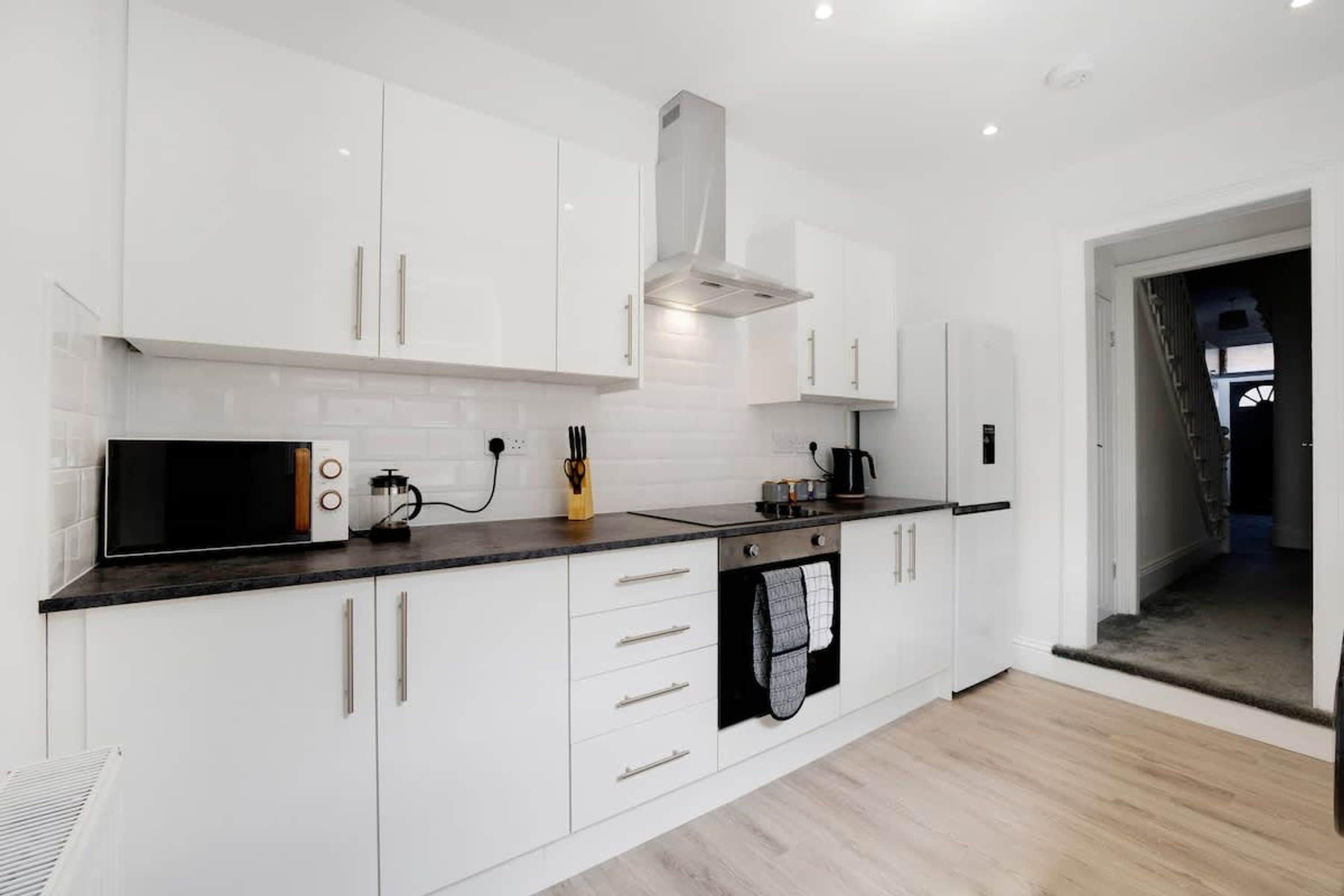 A modern kitchen with white cabinets, a microwave, a coffee maker, and a stove.