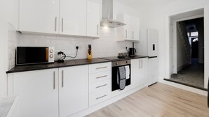 A modern kitchen with white cabinets, a microwave, a coffee maker, and a stove. - 4BR South Shields Stay Sleeps 8 by Stay With Us (South Shields)