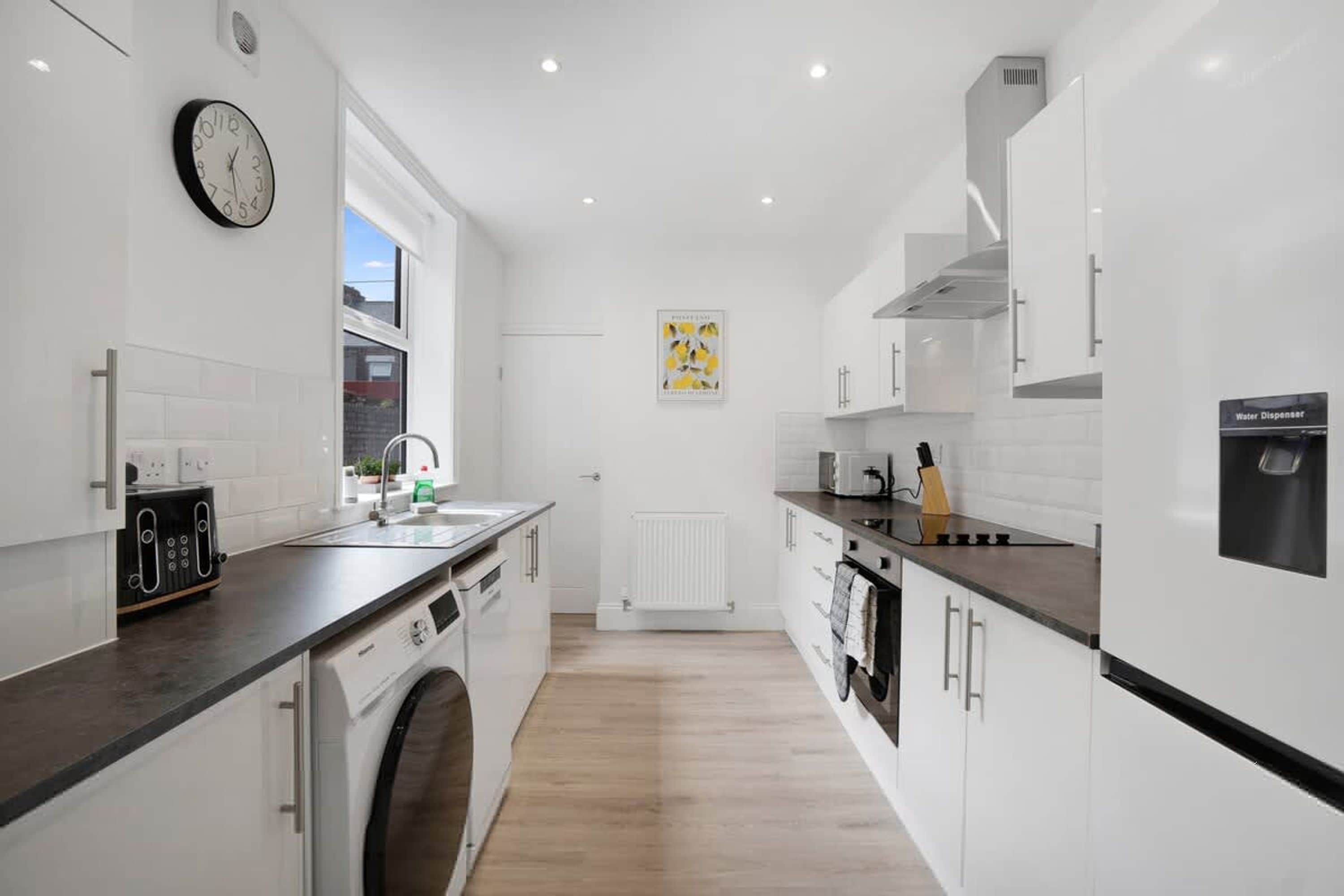 A modern kitchen with a built-in washing machine, a water dispenser, and a clock on the wall.